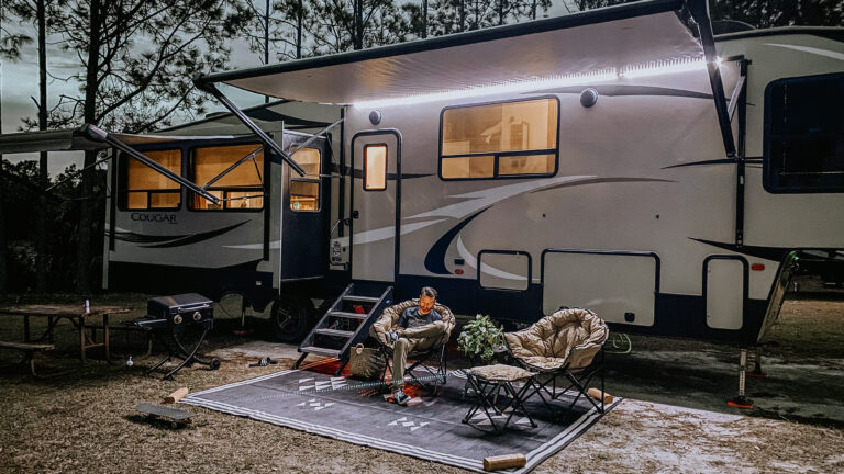 RV trailer with awning and man relaxing underneath