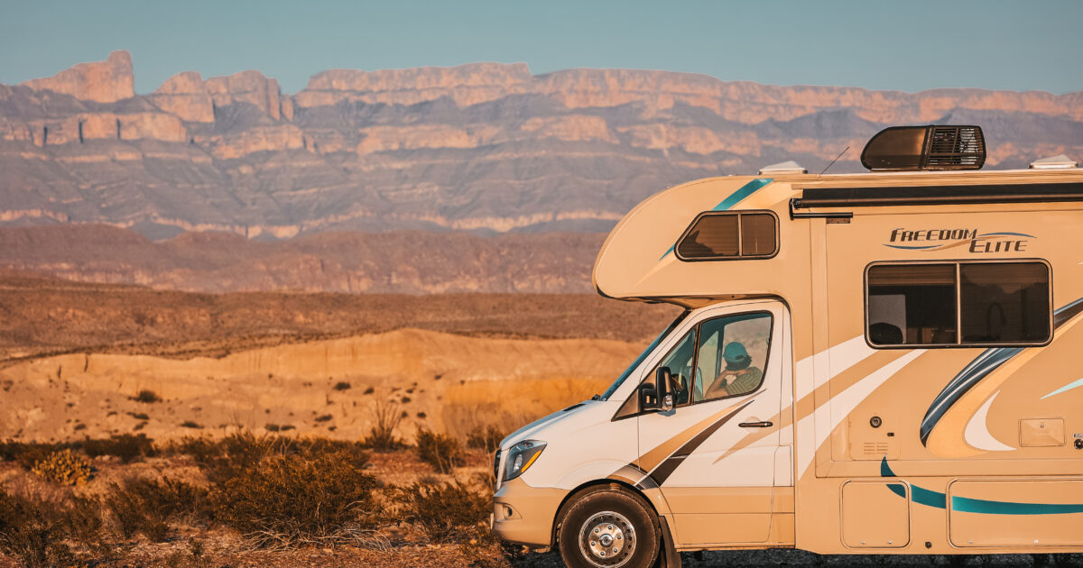 a Class C in front of desert rocks and the setting sun