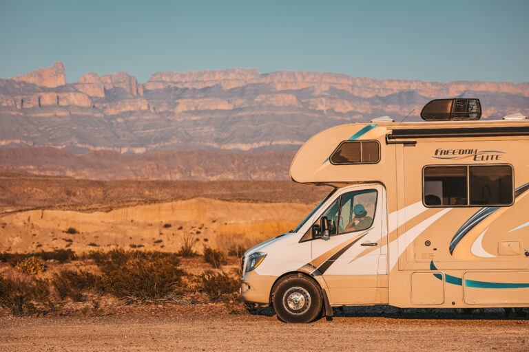 a Class C in front of desert rocks and the setting sun