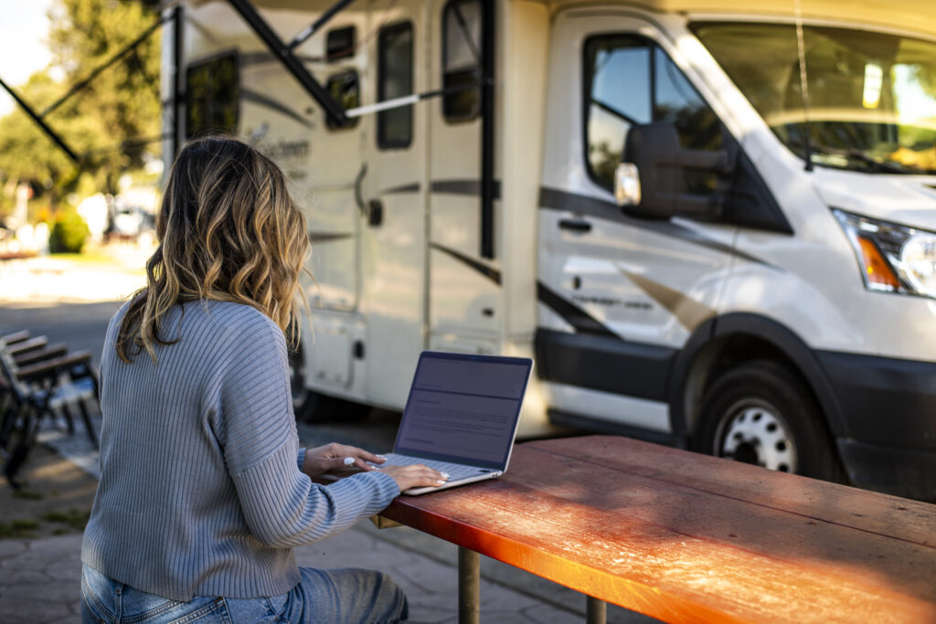 a woman on a laptop next to an RV