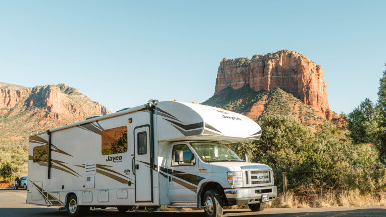 a Class C RV parked in front of red rocks