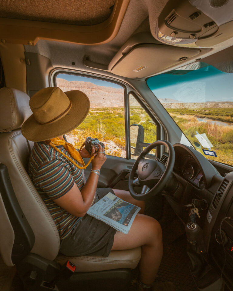 a woman sitting in the drivers' seat of an RV with a camera