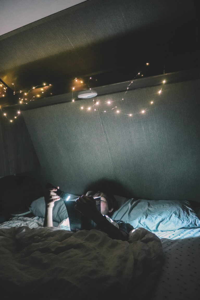 A person reading in bed in an RV with lights on