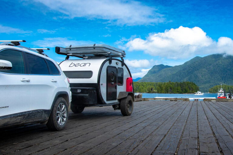 A camper being towed by a car near a lake