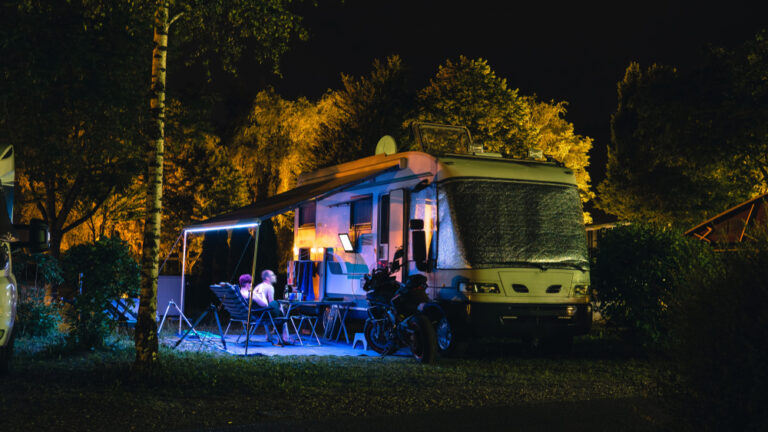 an RV awning lit up at night with people sitting underneath