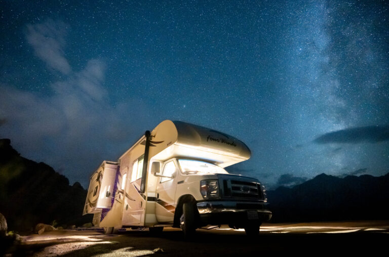 An RV lit up at night under a starry sky