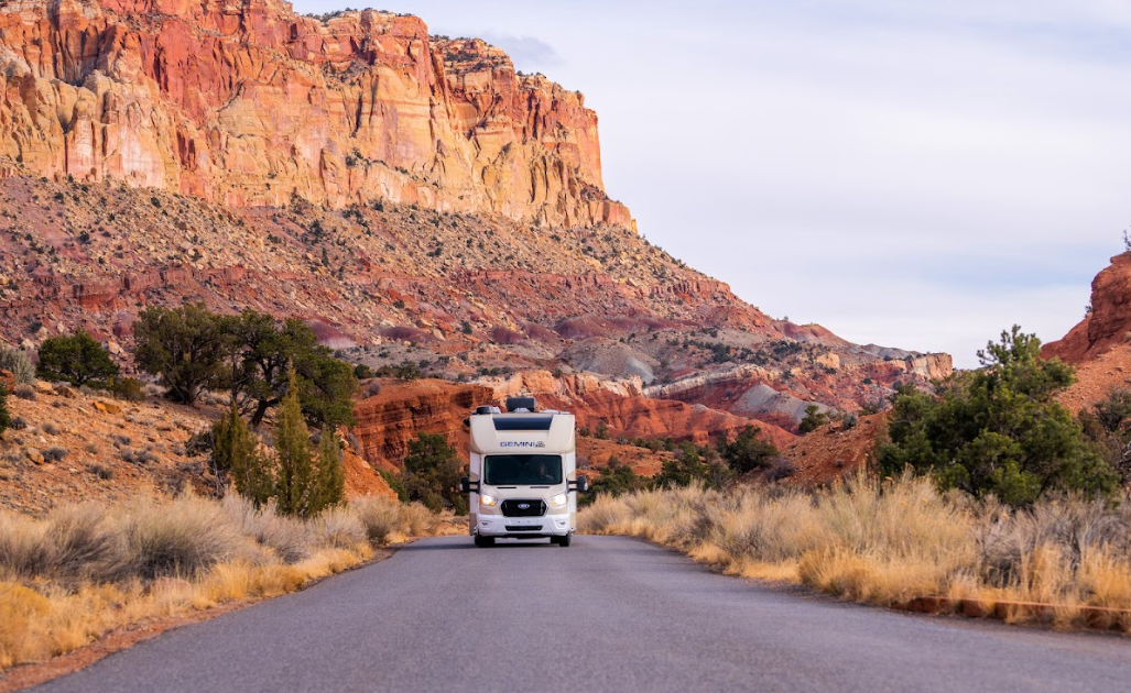 An RV driving down a road in front of red rocks