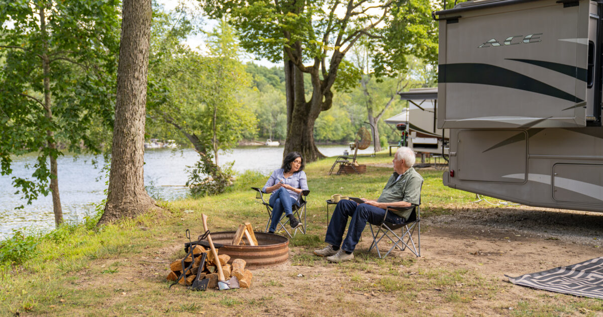 an older couple sitting around a campfire near an RV