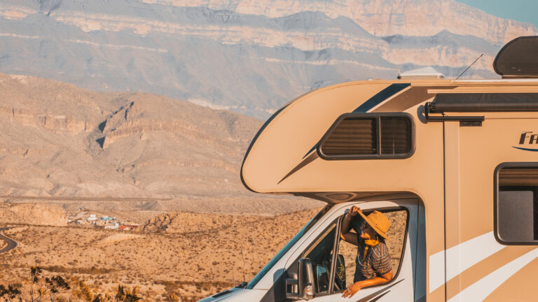 A person looking out the window of an RV in the desert