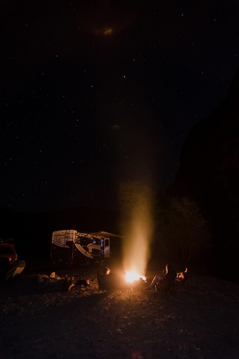 A campfire with an RV illuminated behind it