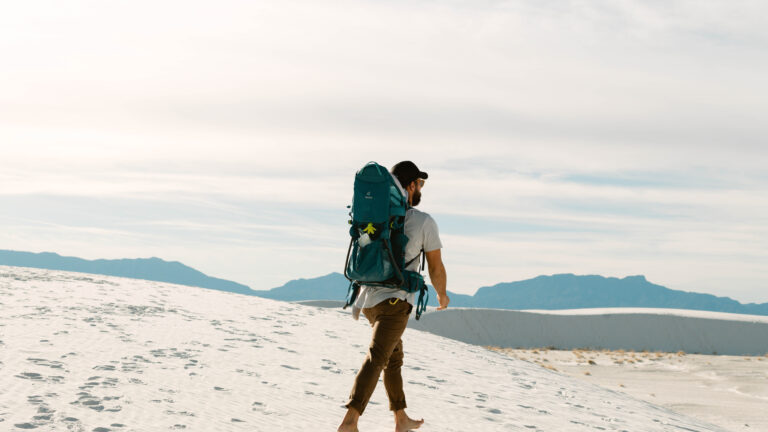 A man backpacking barefoot through the sand