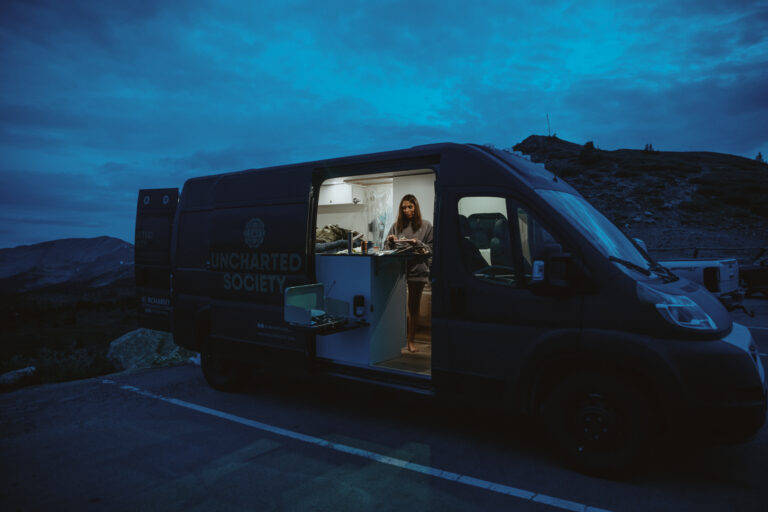 A woman cooking in a Class B camper at dusk