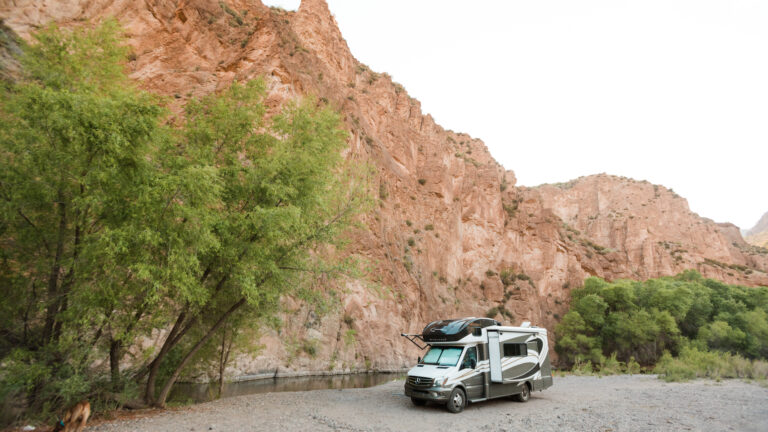 An RV parked by a stream with sheer rocks beyond