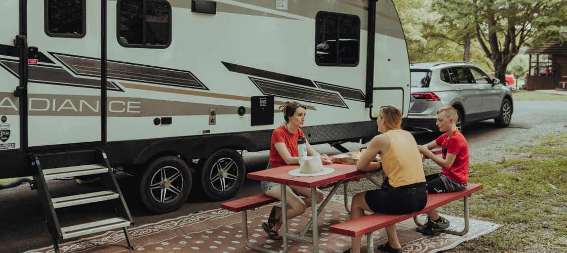 a family at a picnic table in front of their trailer. Full time RVing is a fun way to see the world