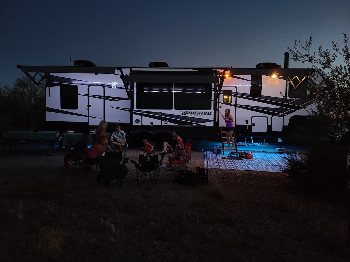 family sitting in a lawn chair circle in front of RV at dusk