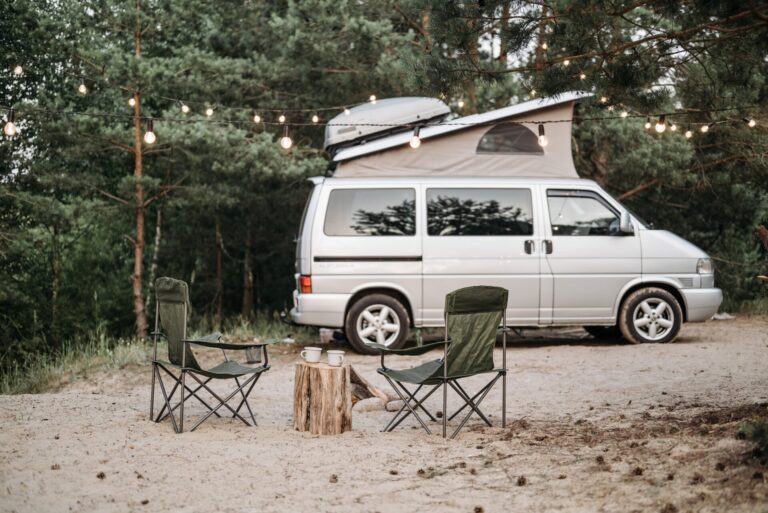 lawn chairs, mugs, and wood placed under hanging lights posed in front of a camper van