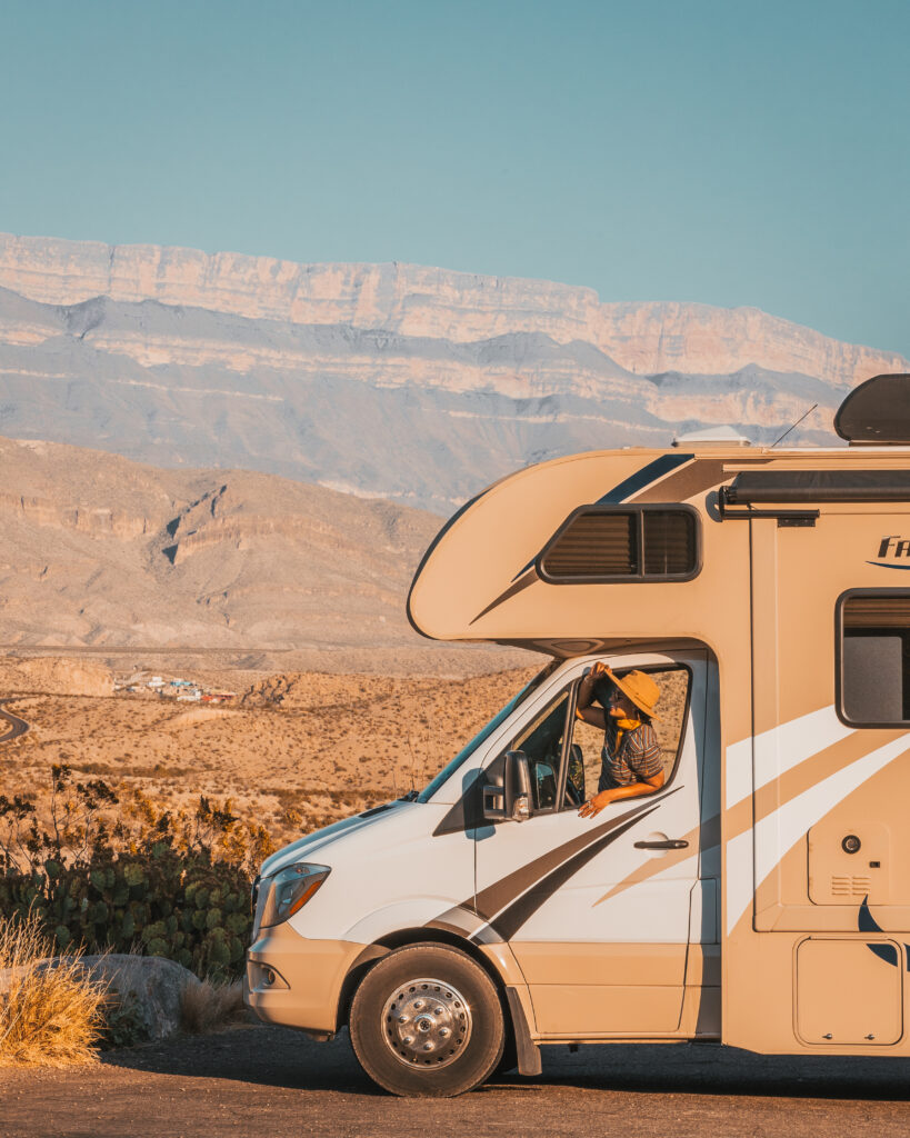 An RV in the desert in front of sheer rocks