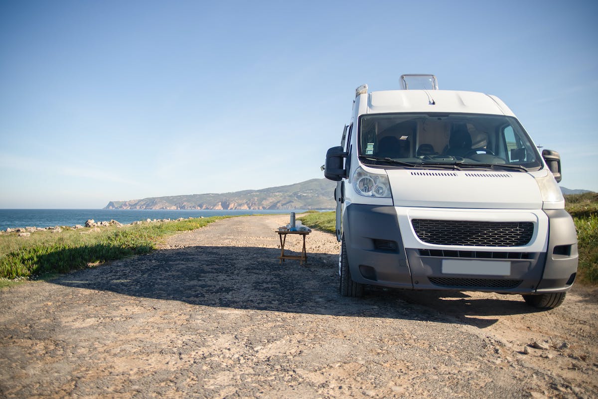 front view of camper van on gravel road by water and mountains