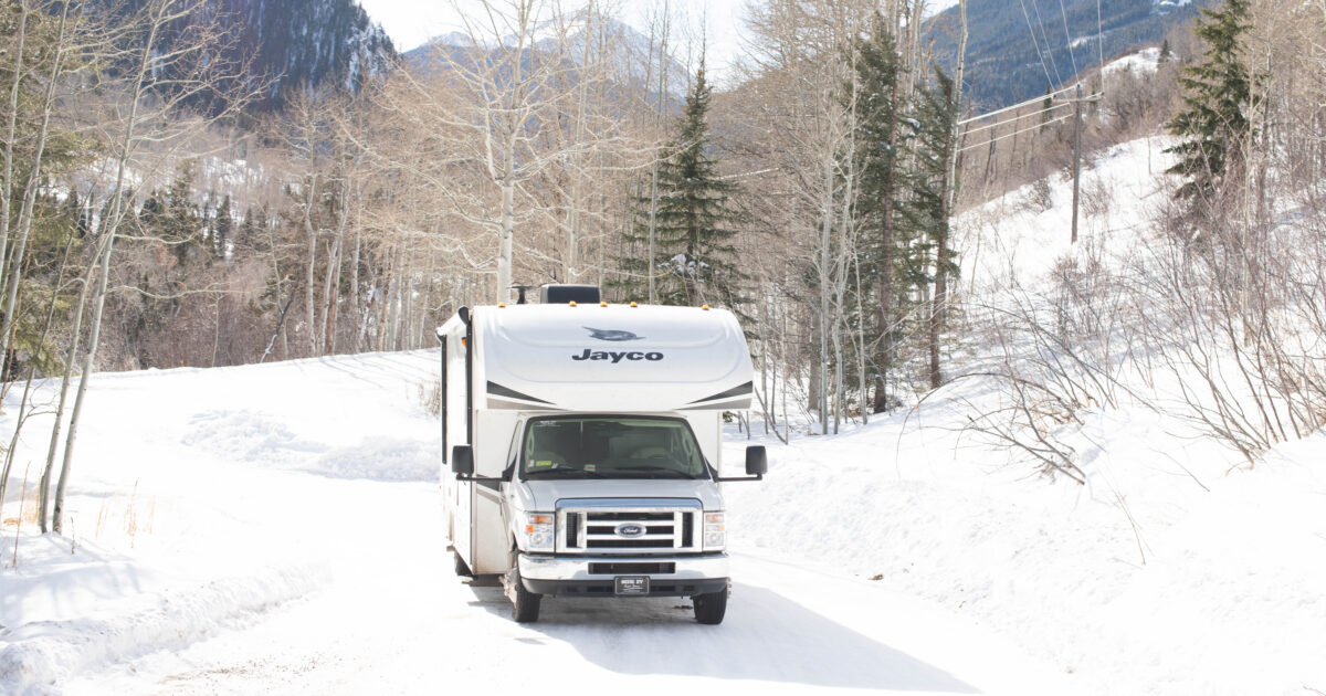 class c rv in the snow with mountains and trees in the background