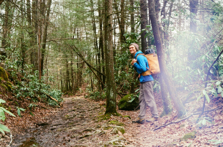 A smiling person hiking in the woods