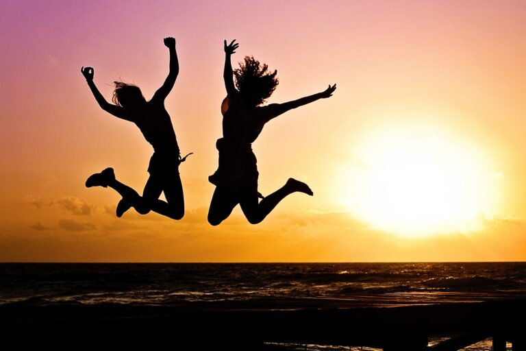 silhouettes of 2 people jumping by beach