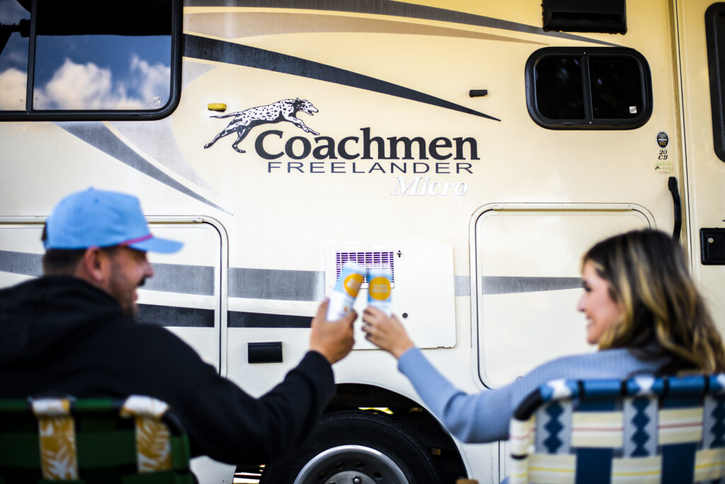 a couple toasting with beers in front of an RV