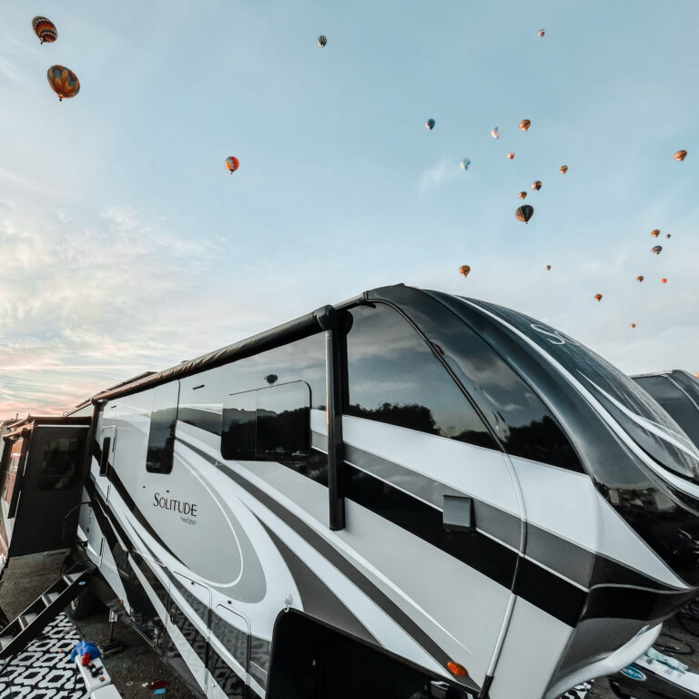 An RV trailer with hot air balloons flying behind it