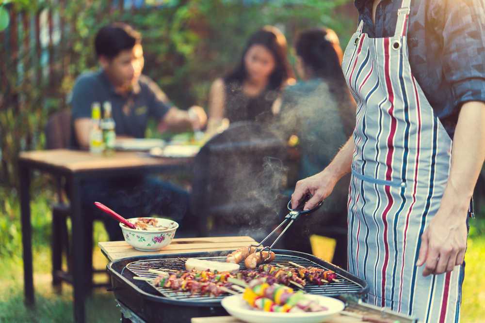 A man barbequing while others eat in the background