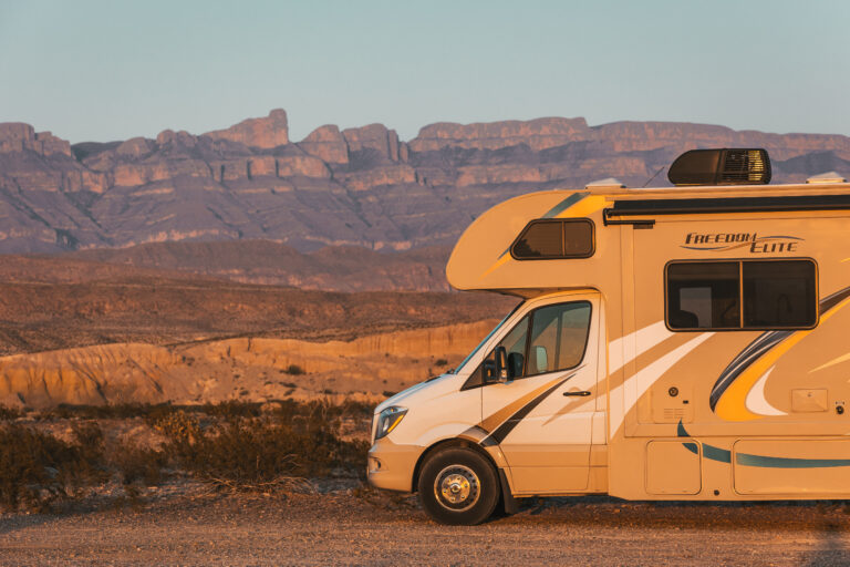 an RV parked by rocky mountains at sunset