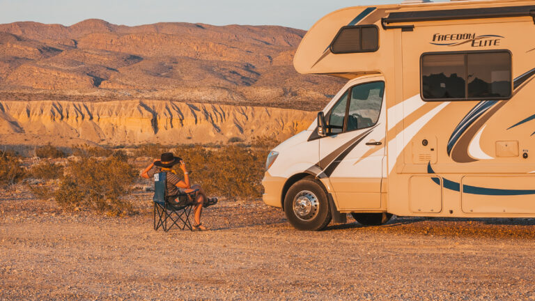a person sitting next to an RV at sunset