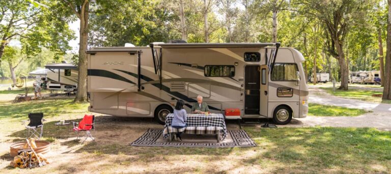 Class A camper set up at campsite with picnic table, two older people playing cards