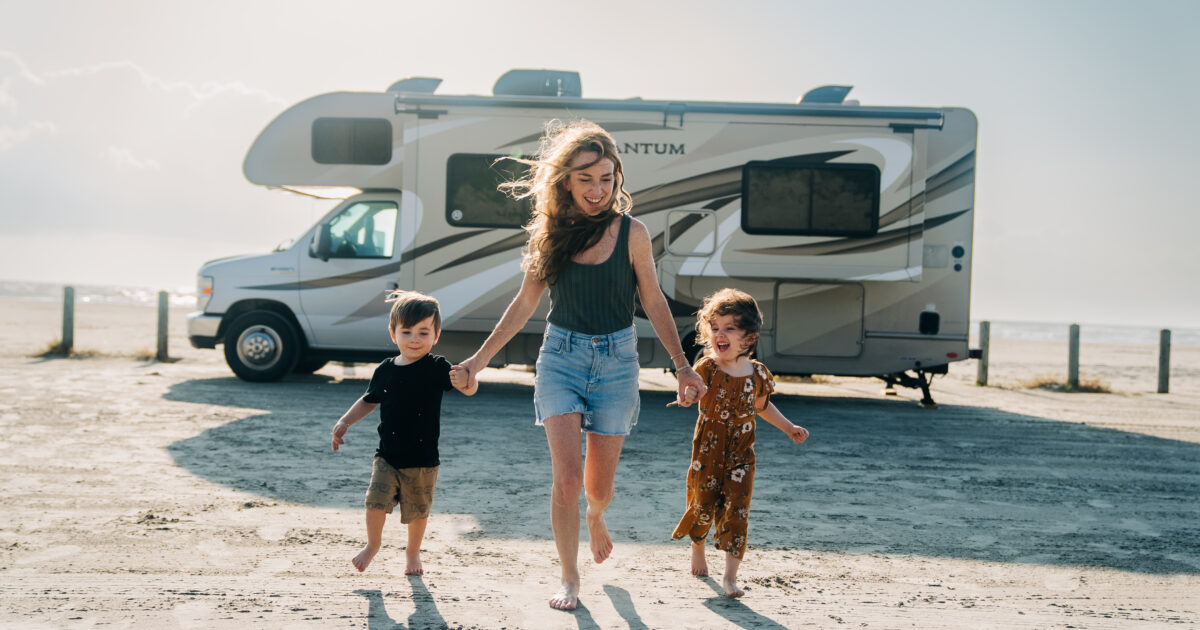 Class C parked on the beach with a family walking in front of it