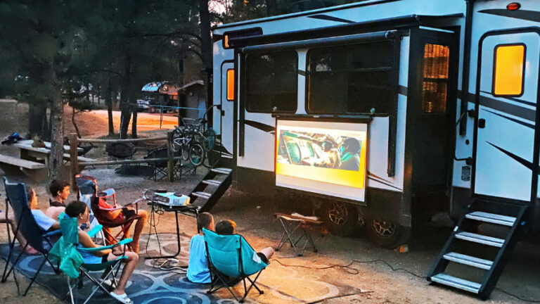 family watching a movie on a projector outside of an rv