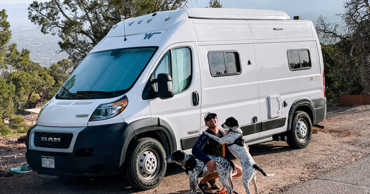 man kneeling in front of a campervan with his two dogs
