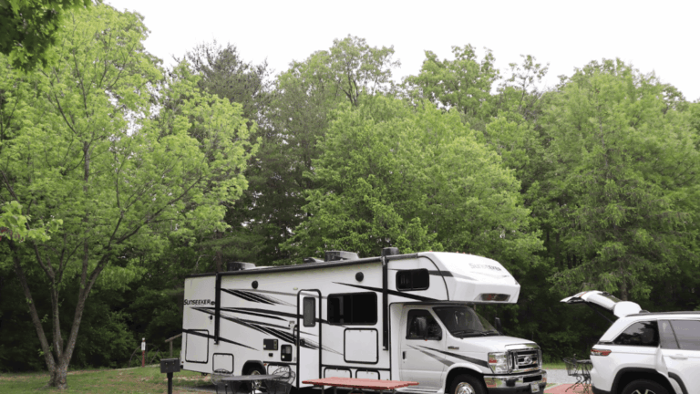 A Class C camper set up next to a car unpacking at a campsite