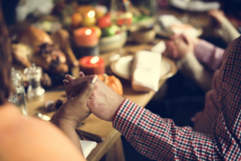 family members holding hands around a Thanksgiving table