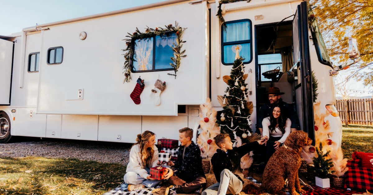 An RV decorated for the holidays with garland and a tree and a family exchanging gifts
