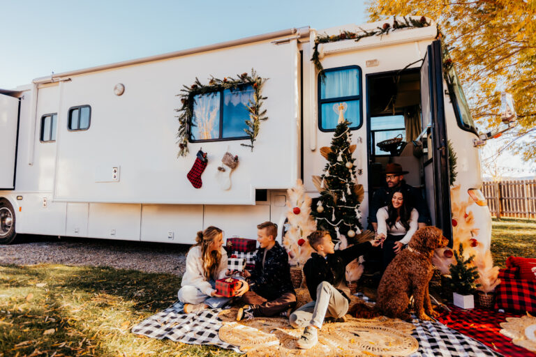 An RV decorated for the holidays with garland and a tree and a family exchanging gifts