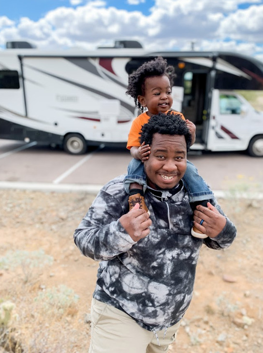 a dad giving son a shoulder ride outside their RV