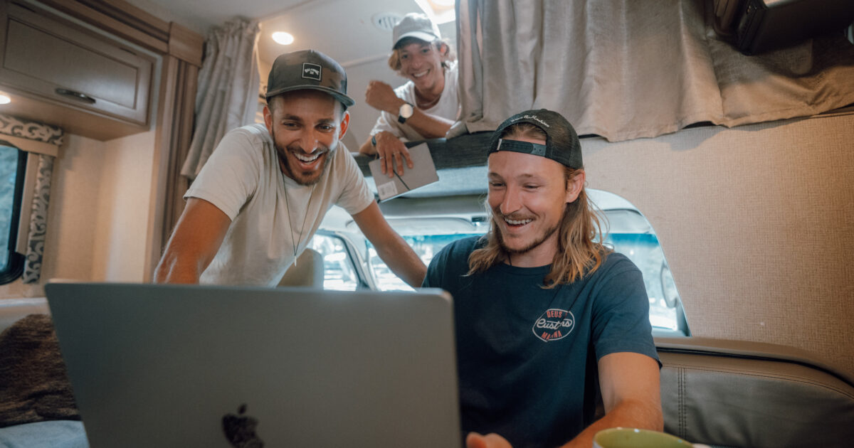 three men on an RV looking at a laptop, planning an RV road trip