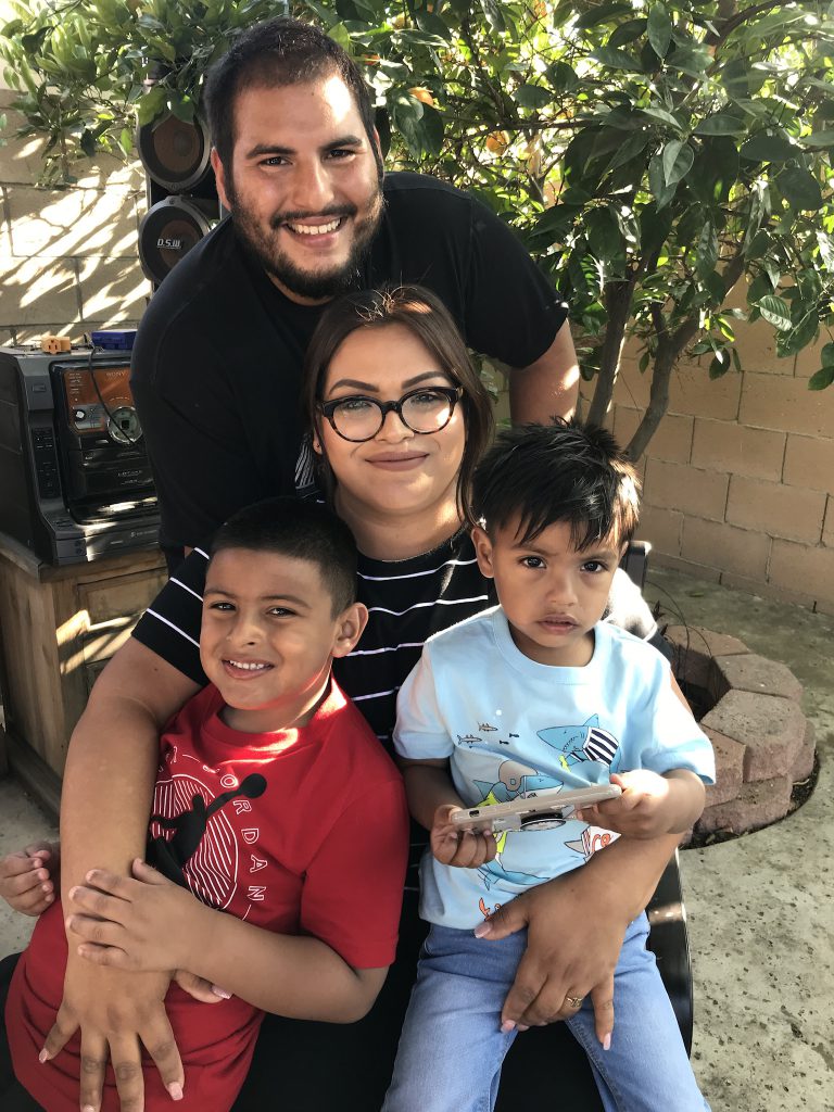 Smiling family of four - two young boys sit on their mother's lap, father stands behind