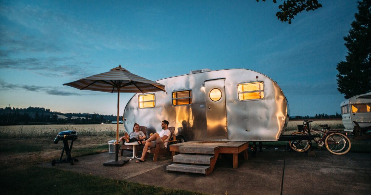 Couple sitting outside a teardrop trailer at twilight