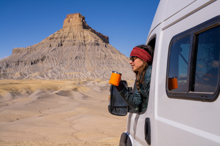 woman dressed for winter leaning out her rv window holding a mug