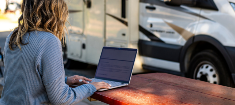 woman looking at laptop at a picnic table in front of an RV