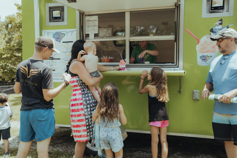 A family (a man, a woman, and three young children) visits a food truck during a vacation