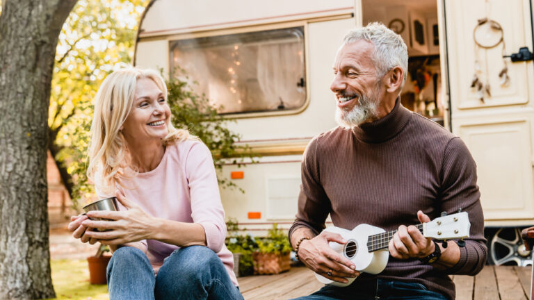 Mature man playing the ukulele for his wife near a campervan
