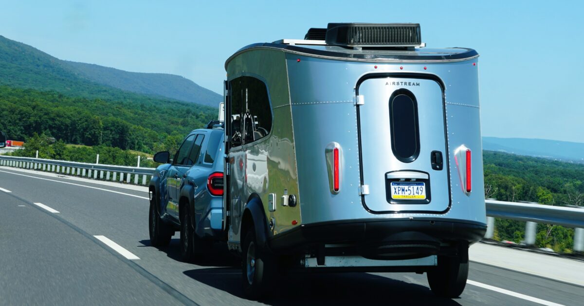 A blue SUV pulls an Airstream travel trailer down a highway bordered by a guardrail.