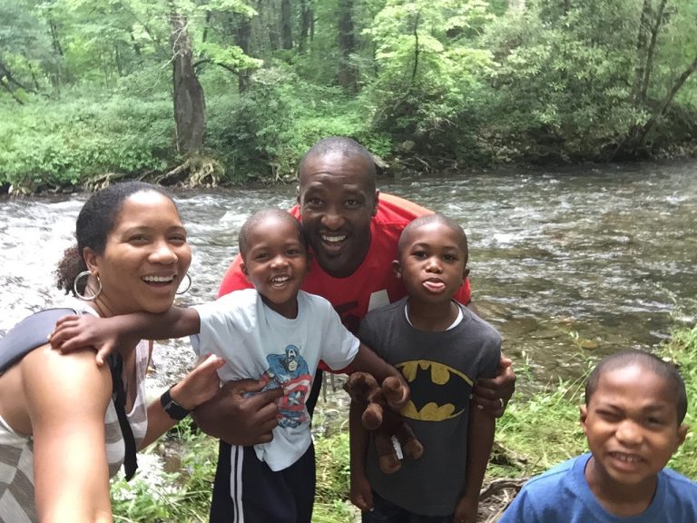 Parents and three young boys smile by a river