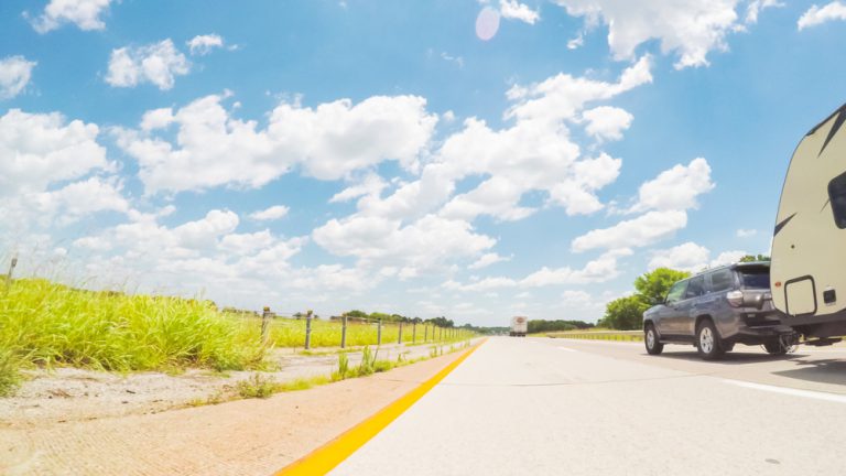 Car and RV trailer driving east in Kentucky under blue skies with patches of white cloud over an unlimited horizon