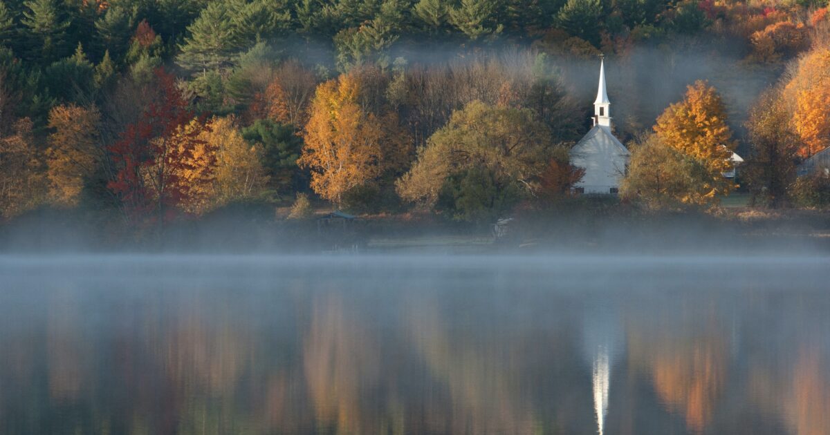 Colorful fall trees and a church across the water, something you might see in New Hampshire
